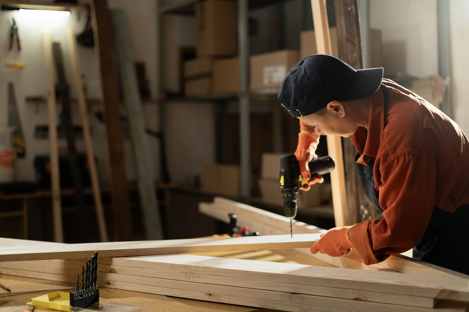 Artisan menuisier dans son atelier utilisant une perceuse électrique sur une planche de bois brut