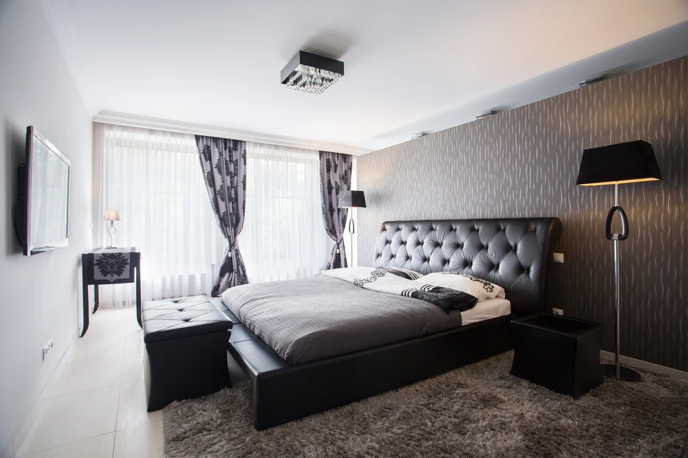 Chambre moderne avec lit double à tête de lit capitonnée en cuir noir, tables de chevet assorties