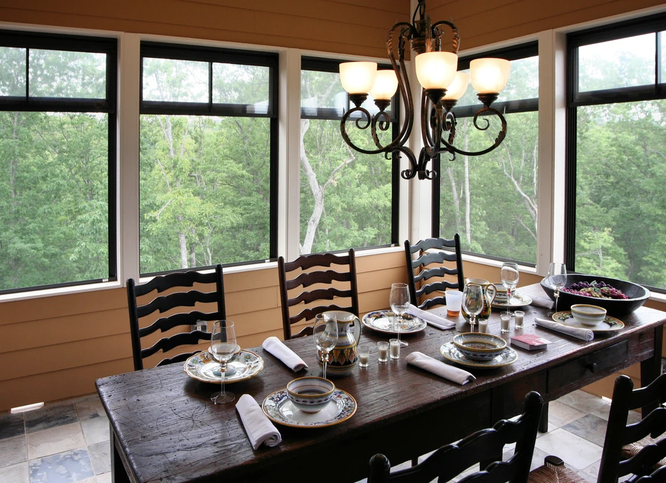 Salle à manger avec table en bois massif dressée pour repas, chaises à dossier à barreaux horizontaux, lustre en fer forgé à abat-jours