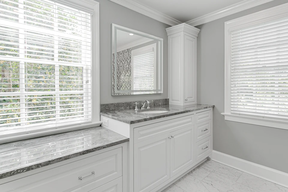 Salle de bain moderne avec mobilier blanc laqué, plan de travail en granit gris veiné, vasque encastrée et robinetterie chromée