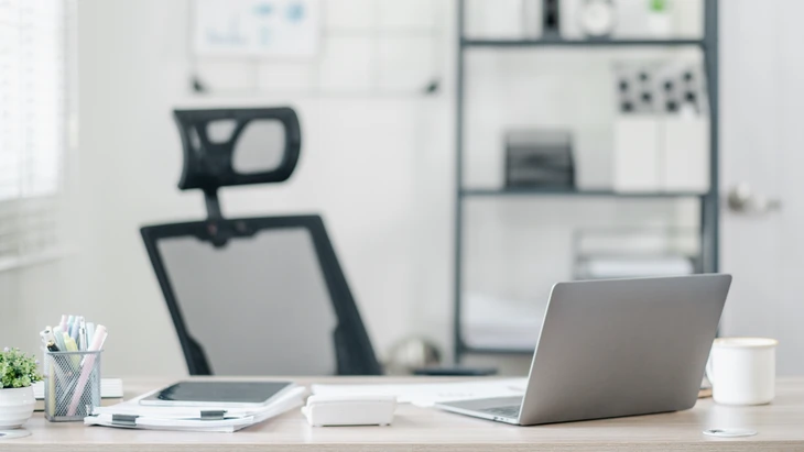Bureau moderne avec chaise ergonomique noire à dossier haut et appuie-tête, ordinateur portable argenté ouvert sur plan de travail en bois clair