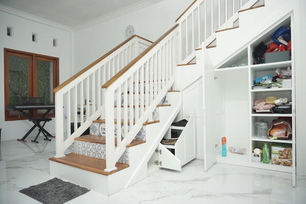 Intérieur moderne avec escalier blanc et bois, rangements intégrés sous l'escalier avec tiroirs coulissants ouverts et étagères murales