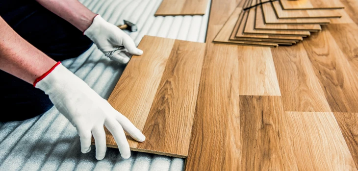 Intérieur d'habitation où un artisan en gants blancs installe du parquet flottant sur sous-couche