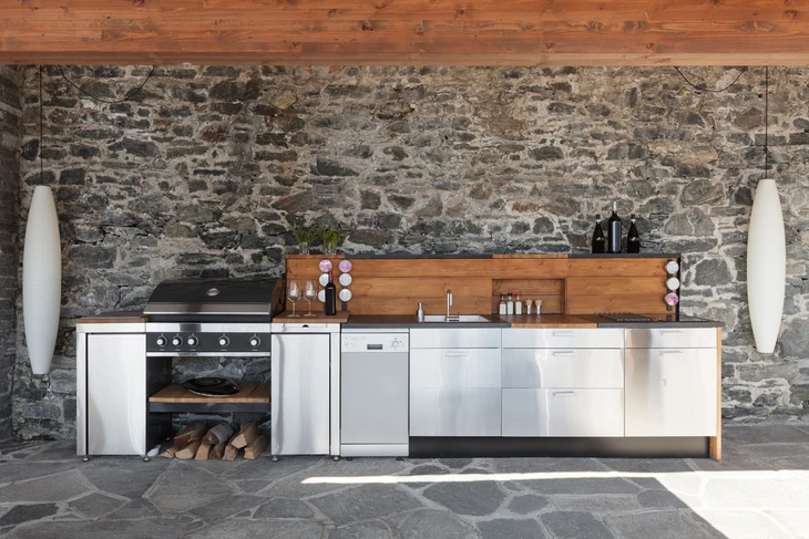 Cuisine moderne intégrée dans un espace rustique avec mur en pierre naturelle apparente et poutres en bois au plafond