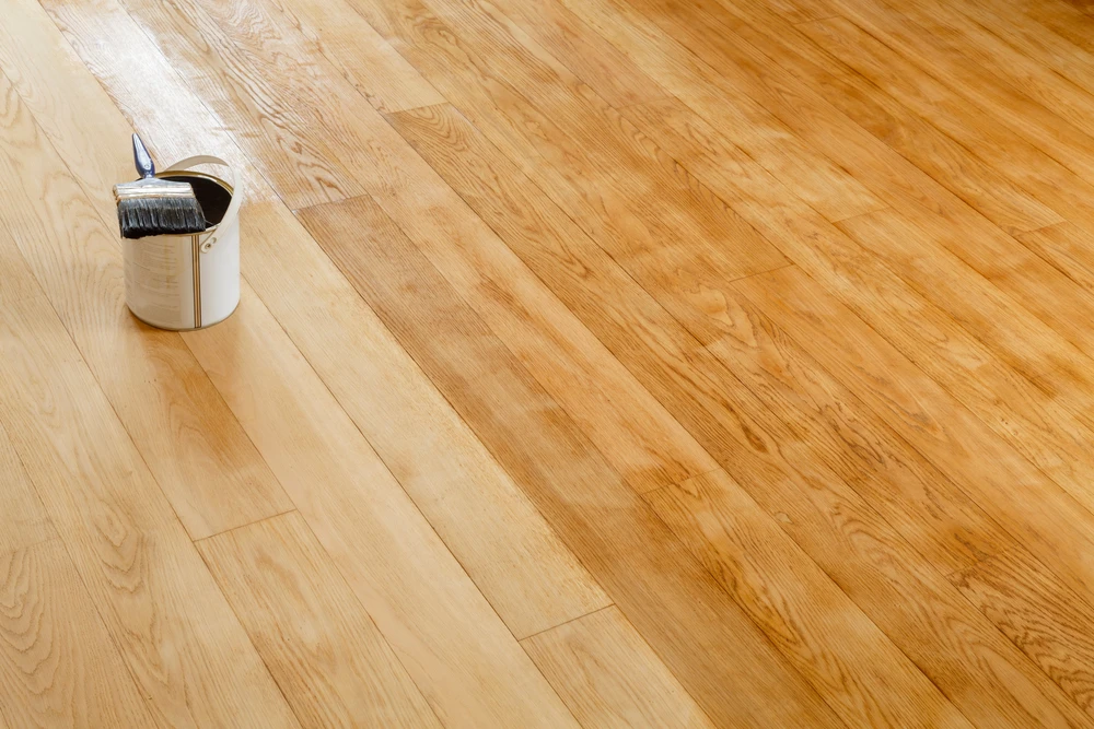 Intérieur montrant un parquet en bois naturel avec pot de vernis ou lasure et pinceau posé au sol