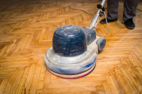 Intérieur résidentiel avec ouvrier effectuant le ponçage d'un parquet en chêne à motif chevron
