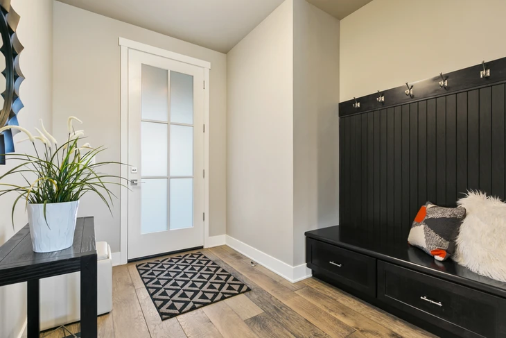 Entrée résidentielle moderne avec banc de rangement intégré en bois noir, crochets muraux et coussins décoratifs