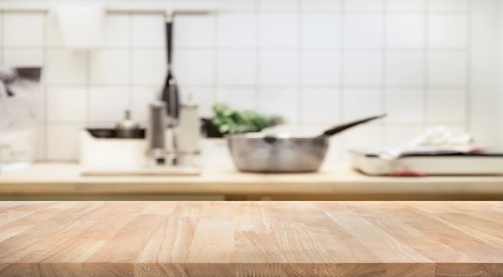 Cuisine moderne avec plan de travail en bois clair au premier plan, évier en inox avec robinetterie contemporaine, ustensiles de cuisson dont casserole et poêle, légumes verts frais, carrelage métro blanc en crédence