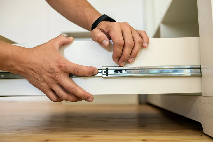 Intérieur moderne avec mains installant une glissière télescopique métallique sur tiroir blanc