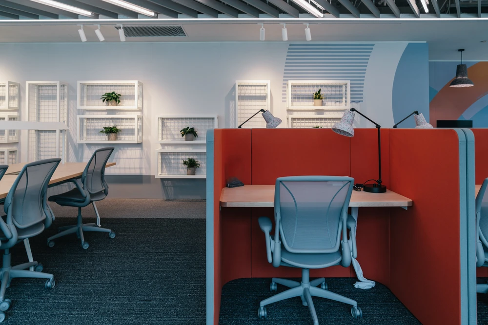 Cet espace de bureau moderne est bien organisé et comprend des postes de travail séparés par des cloisons rouges et grises vibrantes pour une plus grande intimité et une meilleure mise au point