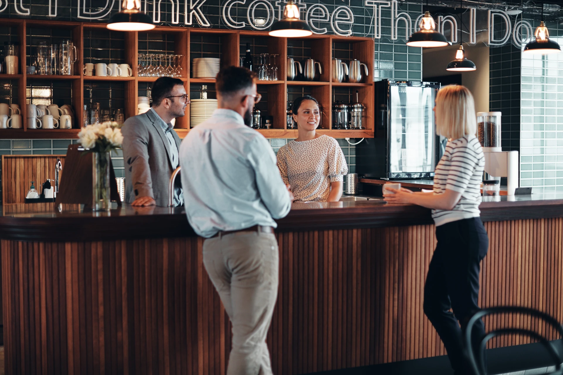 Scène d'entreprise dans un café moderne avec quatre professionnels en réunion informelle au comptoir