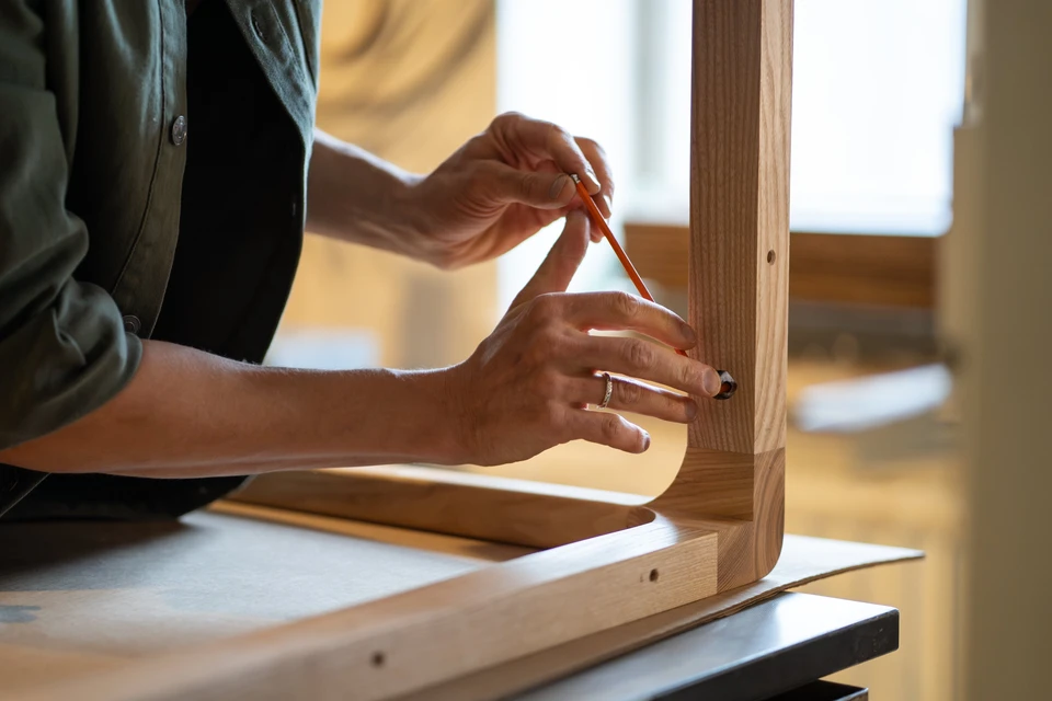 Les mains de menuisier utilisent la clé hexagonale pour visser les boulons, en attachant les pieds de la table au plateau en bois dans l'atelier