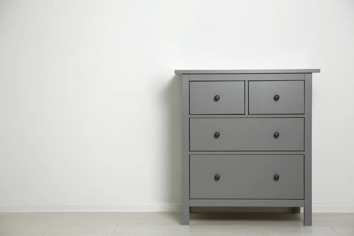 Intérieur minimaliste avec commode grise à quatre tiroirs contre mur blanc