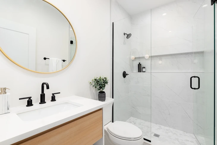 Salle de bains moderne avec armoire en chêne blanc avec plan de travail en marbre blanc, miroir circulaire doré, douche avec hexagone en marbre et carrelage rectangle