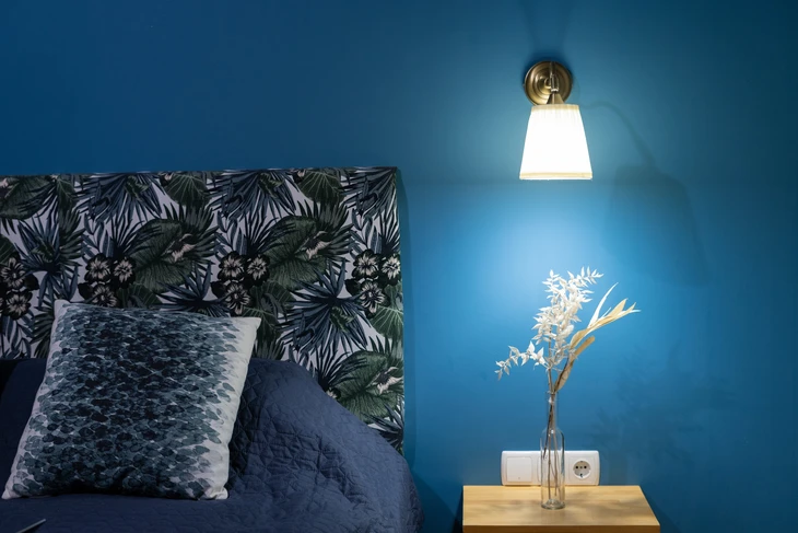 Chambre moderne avec mur bleu profond, tête de lit tropicale à motifs palmiers verts et hibiscus