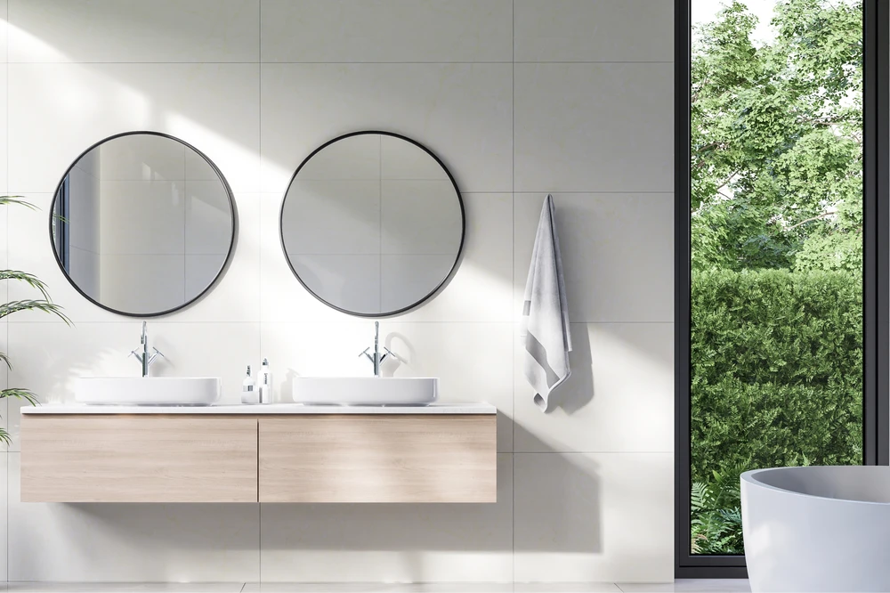 Salle de bains moderne avec double vasque intégrée au plan de toilette blanc, meuble suspendu en bois clair, deux miroirs circulaires à cadre noir