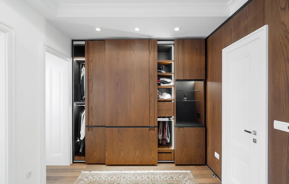 Dressing moderne avec armoires en bois naturel aux portes coulissantes ouvertes révélant rangements intérieurs, étagères et penderies